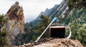 Et JoGO-sugerør lener seg mot en kopp med kaffe høyt oppe på en fjelltopp