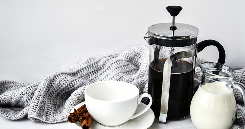 En presskanne med kaffe står på et bord sammen med en kaffekopp og en liten mugge med fløte.