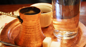 En cezve – en liten kjele – med ferdigbrygget kaffe står på et bord, servert med et vannglass og sukkerbiter