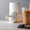 En proteinkaffe i et glass står på et bord sammen med proteinpulver og en shaker