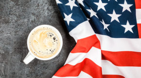 En kopp med kaffe står på et underlag ved siden av et amerikansk flagg