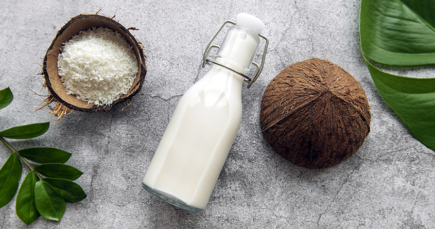 En glassflaske med kokosmelk ligger på en kjøkkenbenk ved siden av to halv kokosnøtter