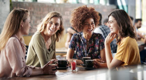 Fire kvinner sitter på en kafé og drikker kaffe og ler