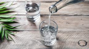 En person heller vann fra en glassflaske over i et glass