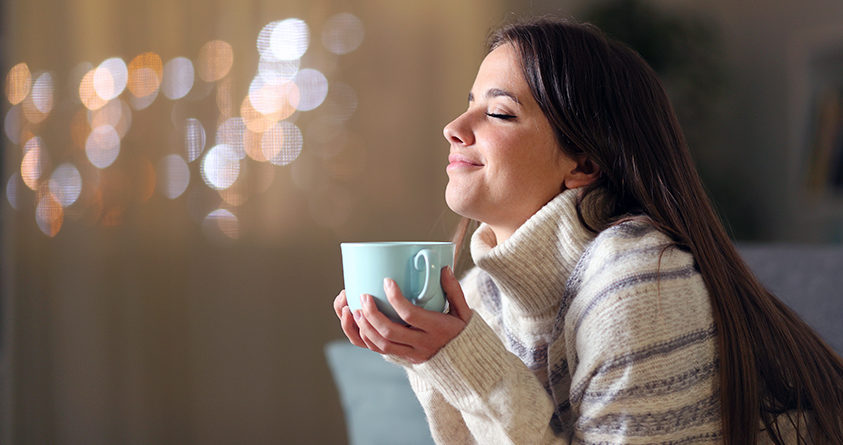 En kvinne smiler og nyter en kopp med kaffe