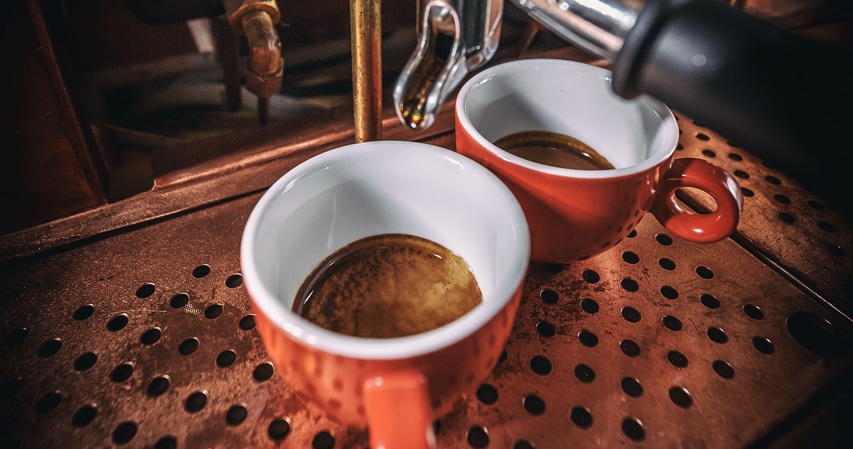 To røde kopper med espresso står under portafilteret i en espressomaskin