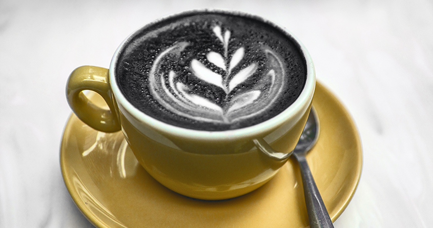 Nærbilde av en charcoal latte med lattekunst i en kopp