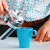 En mann i skjorte heller nytraktet kaffe fra en presskanne over i en turkis kopp