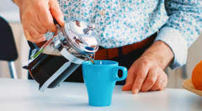 En mann i skjorte heller nytraktet kaffe fra en presskanne over i en turkis kopp