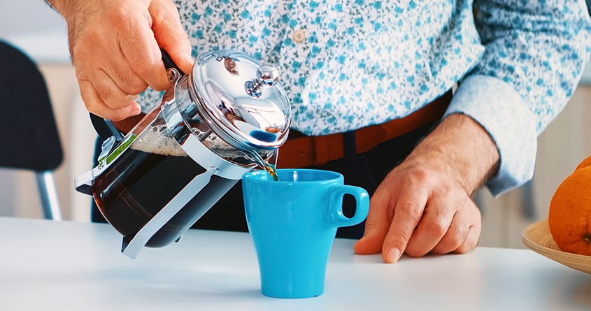 En mann i skjorte heller nytraktet kaffe fra en presskanne over i en turkis kopp