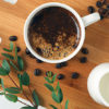 En kopp kaffe står på et skjærebrett sammen med en liten mugge plantemelk
