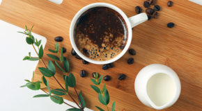 En kopp kaffe står på et skjærebrett sammen med en liten mugge plantemelk