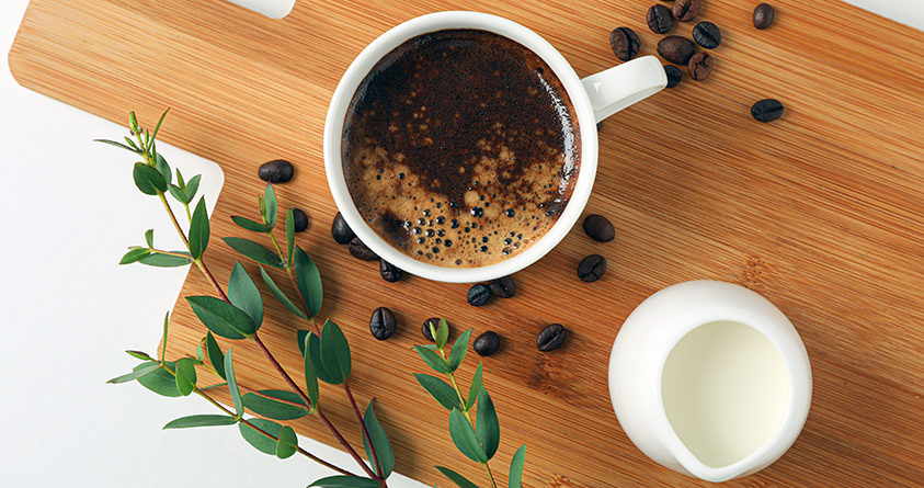 En kopp kaffe står på et skjærebrett sammen med en liten mugge plantemelk