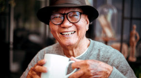 En eldre japansk mann drikker kaffe og smiler mot kameraet