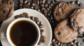 Espressocookies ligger på et bord sammen med en kopp kaffe og masse kaffebønner