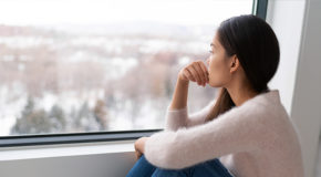 En trist, ung kvinne sitter og ser ut av vinduet