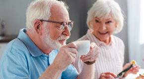 En eldre mann drikker kaffe mens kona hans smiler mot ham