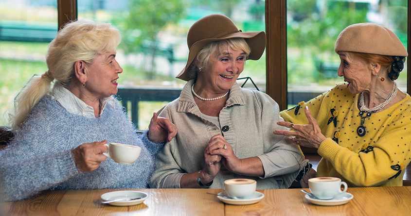 Tre eldre kvinner sitter på kafé og snakker sammen