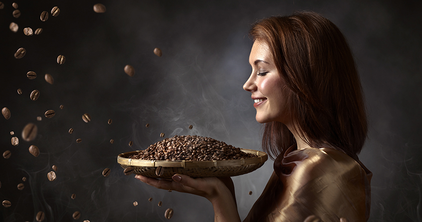 En smilende kvinne holder opp et fat med nybrente kaffebønner