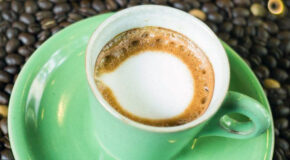En grønn kopp med kaffedrikken espresso macchiato står oppå en seng av kaffebønner