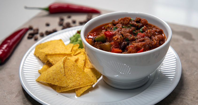 En bolle med chili con kaffe står på en asjett med nachos og guacamole