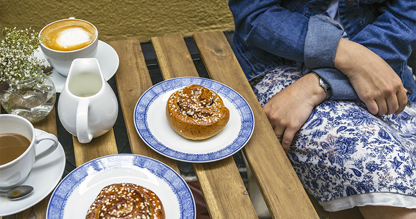 En kvinne sitter på en kafé og nyter kaffe og kanelboller – såkalt fika