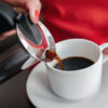 En kvinne heller kaffe fra en perkolator oppi en hvit kopp.