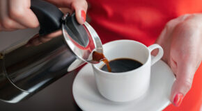 En kvinne heller kaffe fra en perkolator oppi en hvit kopp.