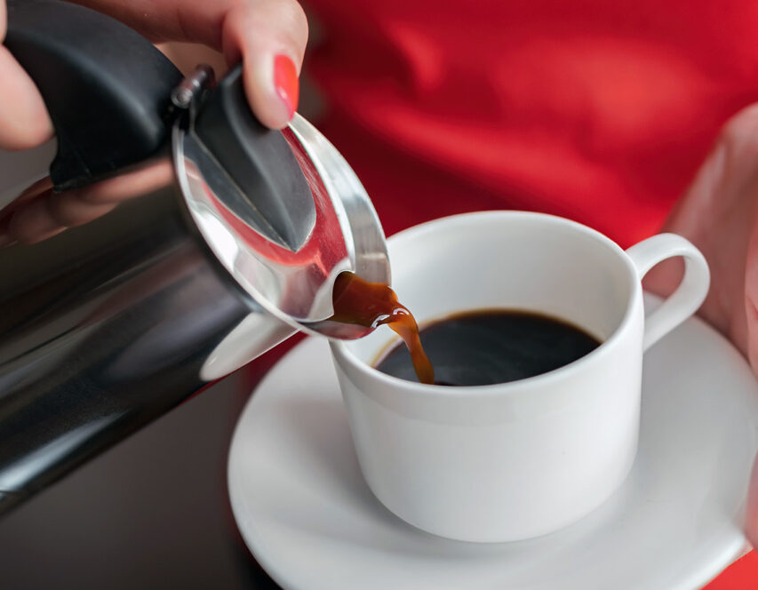 En kvinne heller kaffe fra en perkolator oppi en hvit kopp.