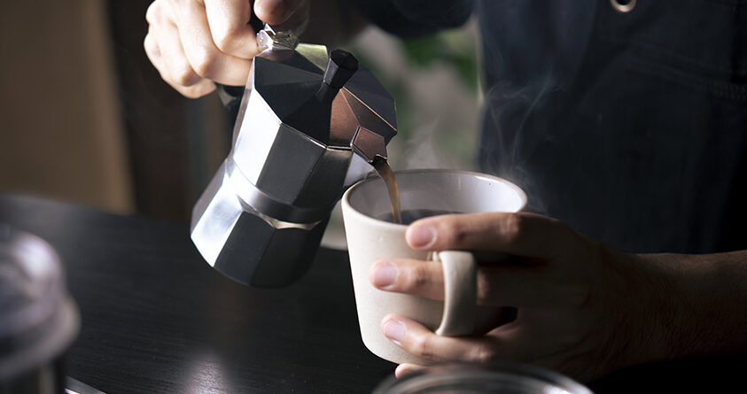 En person heller kaffe fra en perkolator oppi en hvit kopp.
