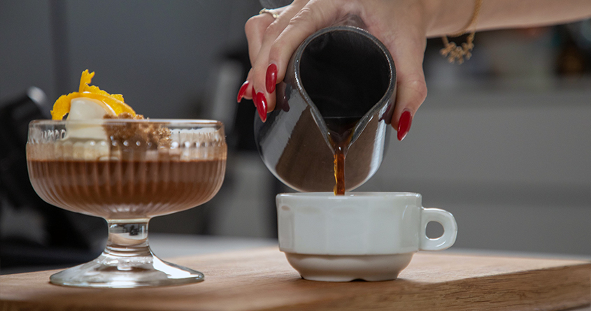 En kvinne heller kaffe i en kopp, ved siden av en skål med mocca pot de crème