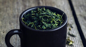 En svart kopp er fylt opp med grønne teblader