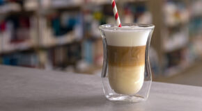Et glass med en cappuccino står på et bord, og man kan se de ulike lagene kaffedrinken består av