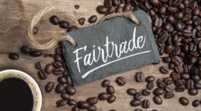 En liten tavle som det står «Fairtrade» på ligger på et bord sammen med kaffebønner og en kopp med kaffe