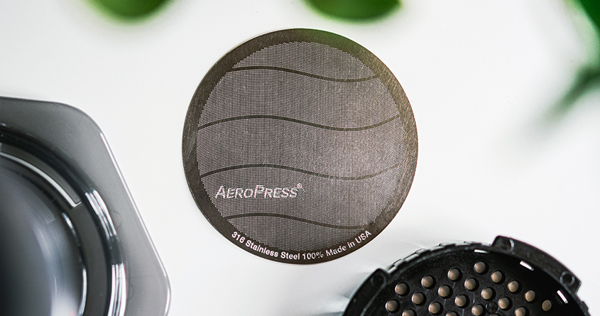 Et AeroPress-metallfilter ligger på en blank overflate