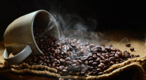 Rykende kaffebønner renner ut av en kopp.