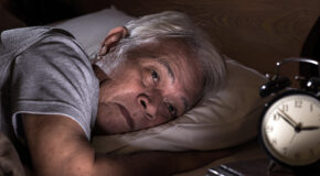 En eldre mann ligger i sengen midt på natten uten å få sove.