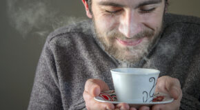 En mann holder en kopp kaffe opp mot ansiktet og smiler