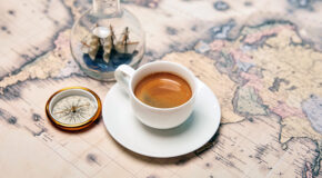 En kopp med kaffe står på et gammelt kart ved siden av et kompass og et skip i en lyspære