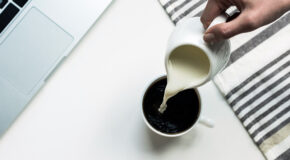 En person heller melk fra en liten mugge oppi en kopp med kaffe