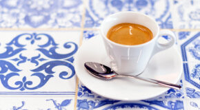 En kopp med café com cheirinho står på hvite- og blåmønstrede fliser