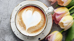 En kaffekopp med et hjerte som lattekunst står på et bord ved siden av tulipaner