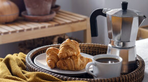 En tallerken med croissanter står på et brett sammen med en mokkakanne og en kopp kaffe