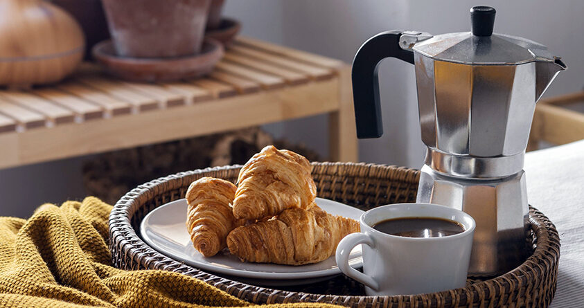 En tallerken med croissanter står på et brett sammen med en mokkakanne og en kopp kaffe