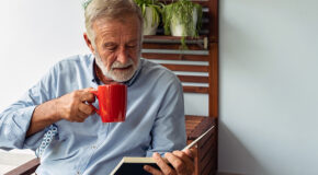 En eldre mann leser en bok og drikker kaffe