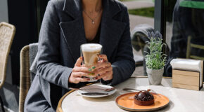 En kvinne sitter på kafé og holder et glass med galão