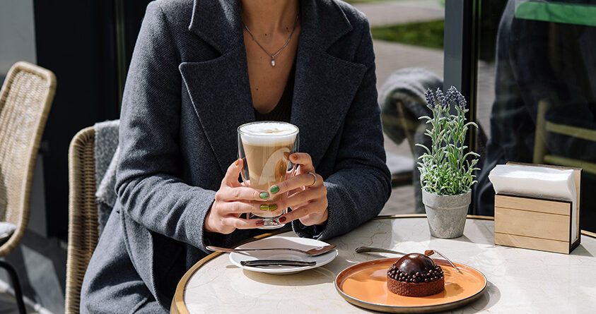 En kvinne sitter på kafé og holder et glass med galão