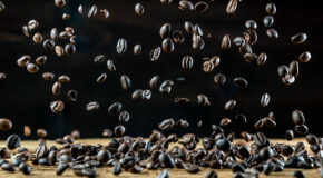 Masse kaffebønner faller ned på et trefarget underlag