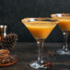 To glass med pumpkin spice espresso martini står på en kjøkkenbenk ved siden av et par gresskar