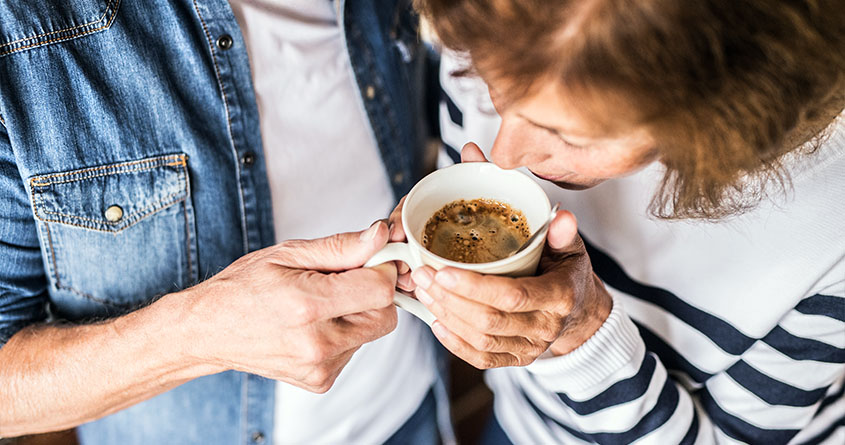 En kvinne lukter på en kopp med kaffe som en mann holder opp